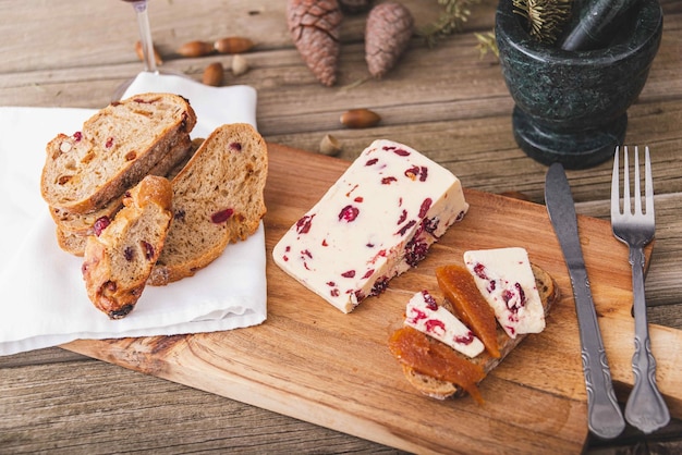 Queso Wensleydale con arándanos, vino tinto, miel, nueces, pasas sobre tabla de cortar de madera, fondo de hormigón negro, enfoque selectivo