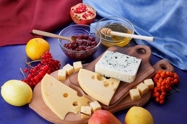 Quesos con miel y limón sobre un fondo azul con servilletas azules y rojas Dos tipos de queso sobre una tabla de madera con frutas y bayas de cerca