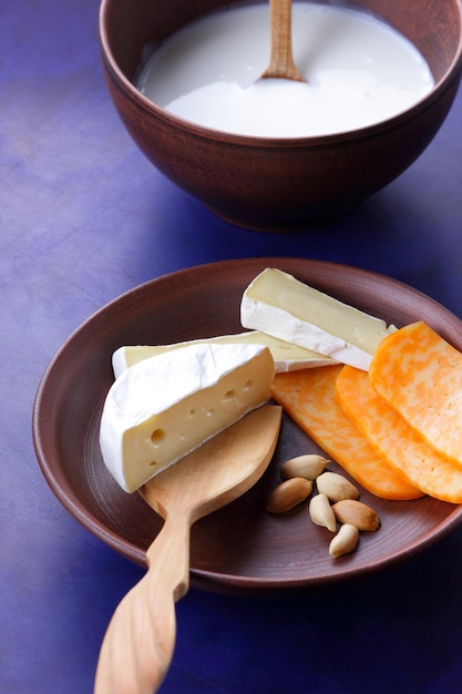 Quesos con nueces y una espátula de madera sobre un plato de arcilla Diferentes tipos de plato de queso y un tazón de leche sobre un fondo azul cerrado