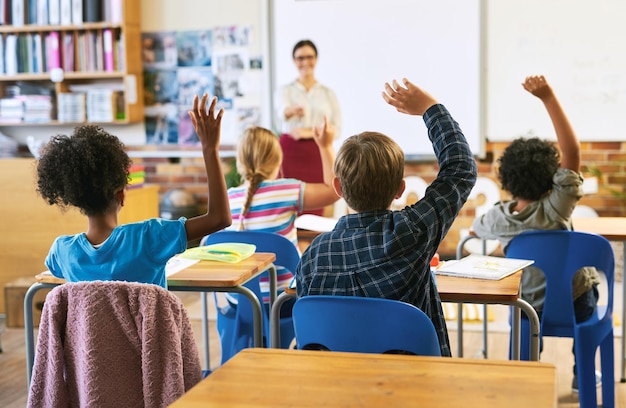 Questão educacional com um grupo de crianças na sala de aula e levantam as mãos para responder Aprender ou apoiar a diversidade e o ensino do professor com jovens alunos na classe do prédio da escola juntos