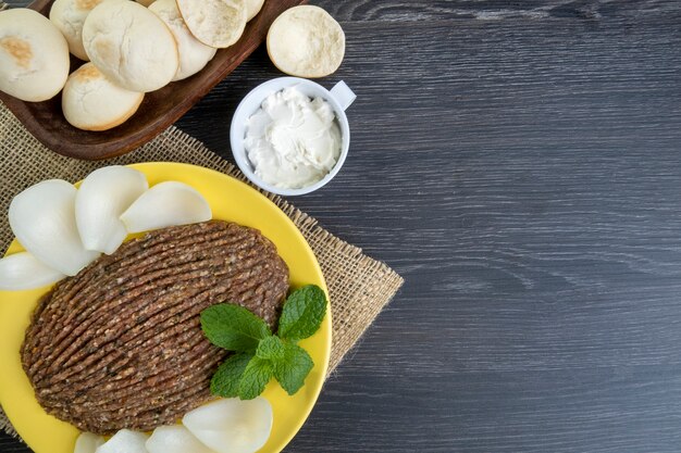 Quibe cru com cebola fatiada, requeijão seco, pão sírio e folhas de hortelã.