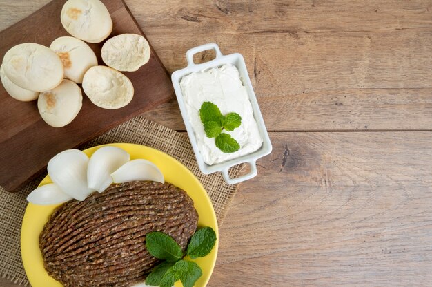 Quibe cru com cebola fatiada, requeijão seco, pão sírio e folhas de hortelã.