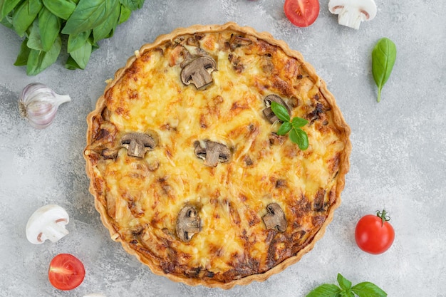 Quiche com cogumelos e frango em um recheio cremoso sobre um fundo cinza de concreto.