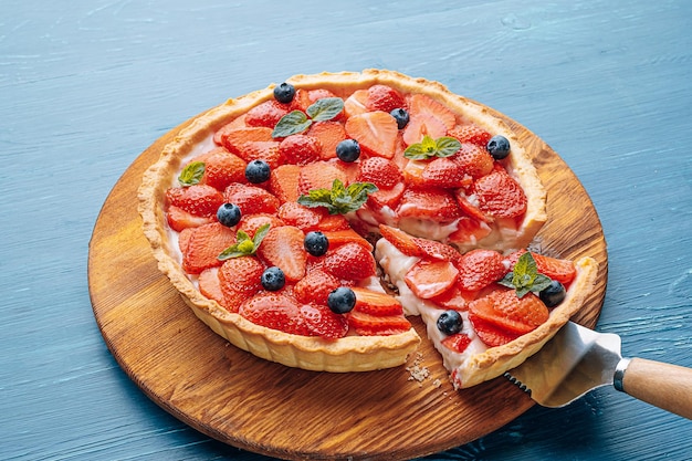 Quiche com raspas de limão e fatias de morango com mirtilos e folhas de hortelã fresca em uma mesa de madeira azul uma fatia é cortada da torta e está pronta para servir