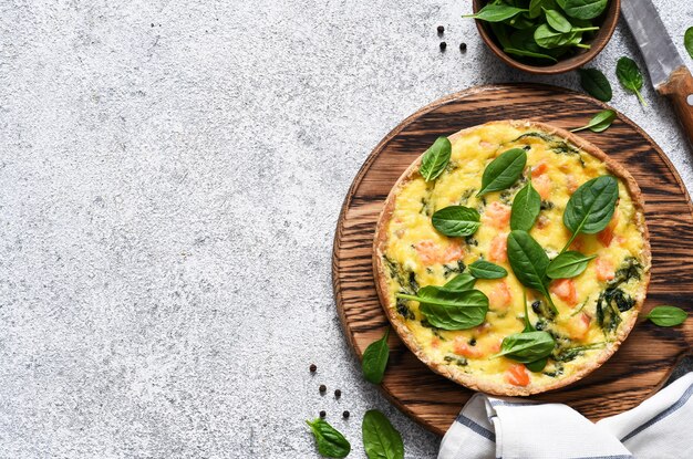 Quiche com salmão e espinafre, queijo em um fundo claro de concreto. Vista de cima.