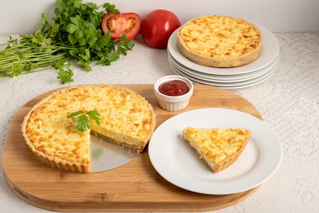 Quiche de queijo uma torta em uma tábua de madeira uma fatia da torta em um prato branco