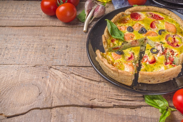 Quiche lorraine caseira, torta saborosa com salmão, brócolis, espinafre e tomate, na mesa de madeira