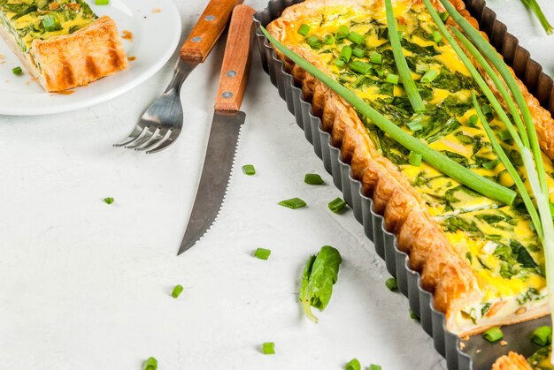 quiche lorraine de hojaldre, con cebollas verdes jóvenes y espinacas En mesa de hormigón blanco