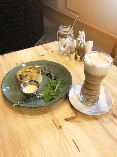 Quiche Lorraine mit Wurst und Rucola auf dem Teller und Latte-Kaffee auf dem Tisch im Restaurant