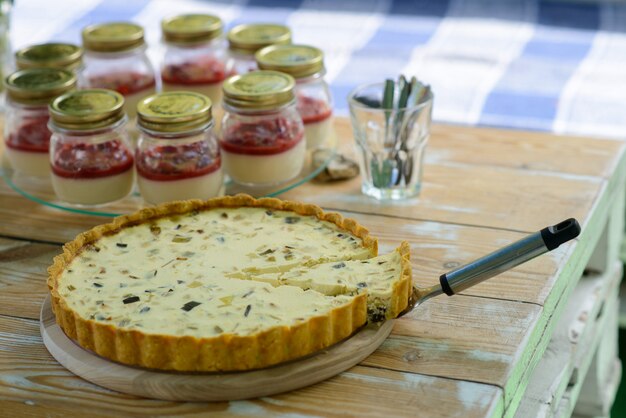 Quiche lorraine pie mit geschnittener scheibe auf einem holztisch mit gläsern mit pannacotta.