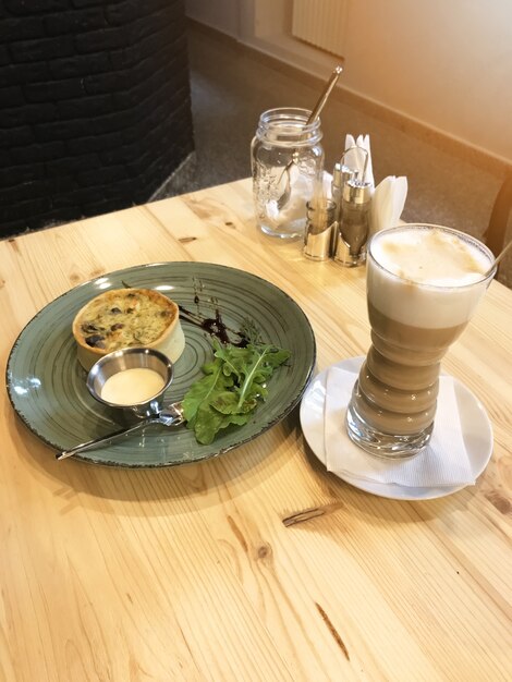 Foto quiche lorraine con salchicha y rúcula en el plato y café con leche servido en la mesa en el restaurante