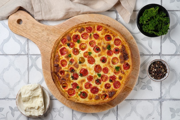 Quiche mit Hühnchen, Kirschtomaten und Käse. Appetitlich offener französischer Kuchen. Auf einem Küchenbrett aus Holz anrichten. Sicht von oben.