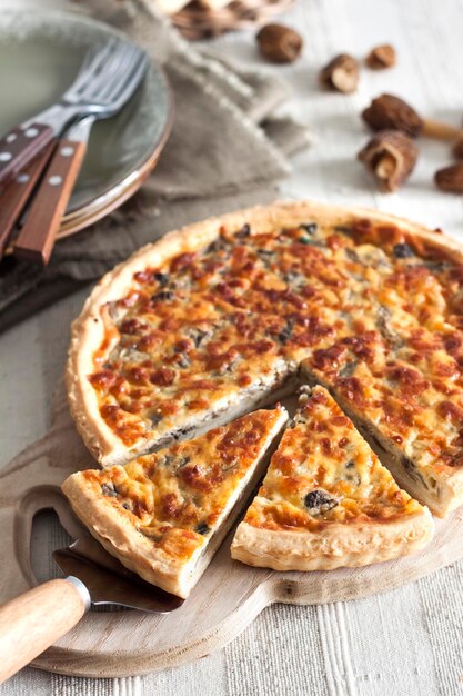 Quiche offener Tortenkuchen mit Morcheln, Zwiebeln und Käse auf Holzschneidebrett