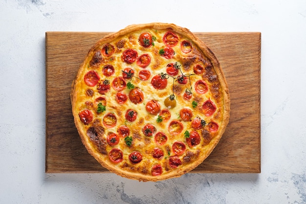 Quiche de pollo, tomates cherry y queso. Apetitosa tarta francesa abierta. Plato sobre una tabla de madera sobre la mesa de la cocina. Horizontalmente.