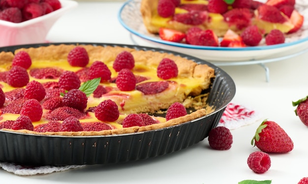 Quiche redondo con fresas rojas y frambuesas en una vista de mesa blanca