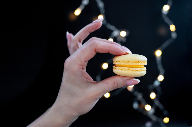 Foto quiero macarrones, mano femenina sostiene macarrones sobre fondo negro