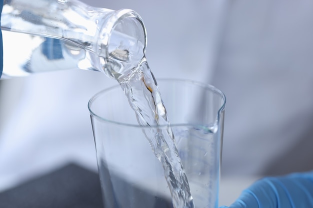 Químico científico vertiendo agua de botella transparente en matraz en primer plano de laboratorio
