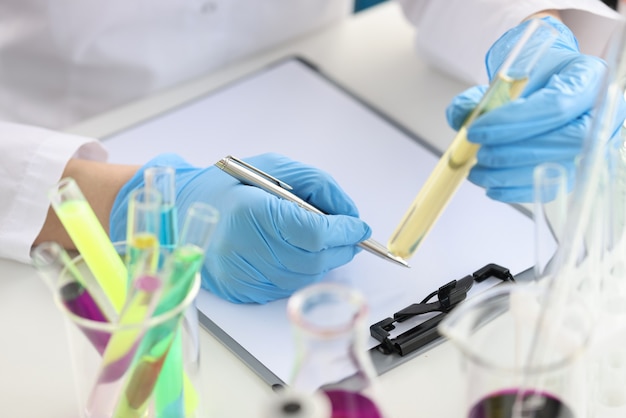 Químico de cientista segurando um tubo de ensaio com um líquido amarelo nas mãos e escrevendo em documentos closeup.