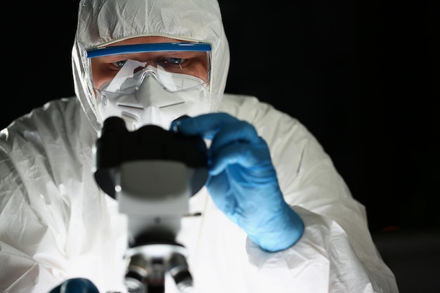 Foto químico de pessoa concentrada em luvas de proteção azuis olha para microscópio no laboratório de química