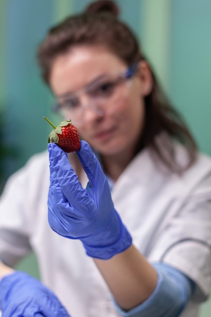 Químico con gafas médicas mirando fresas inyectadas con pesticidas químicos examinando frutas para el experimento del investigador agrícola