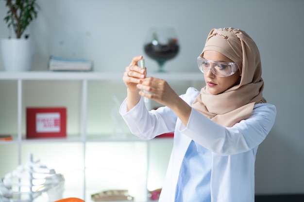 Químico inteligente. Química inteligente usando óculos de proteção e um hijab segurando um tubo de ensaio