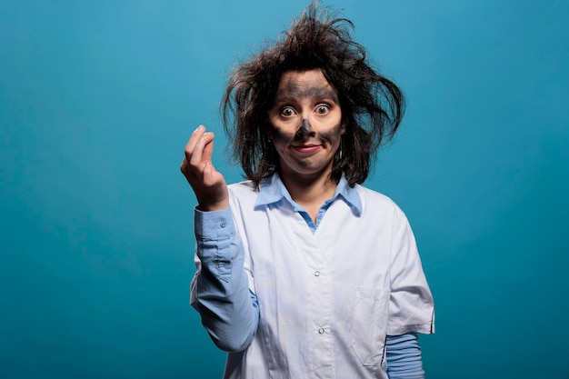 Químico louco olhando bobo com cara suja e cabelo bagunçado, olhando para a câmera sobre fundo azul. Cientista louco com hilário e engraçado cuida da explosão química do laboratório. Tiro de estúdio.