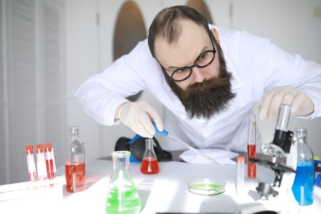 Químico louco. Um cientista louco conduz experimentos em um laboratório científico. Realiza pesquisas usando um microscópio.