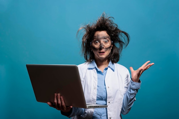 Químico lunático com cabelo bagunçado e rosto sujo com laptop enquanto gesticula com raiva após explosão perigosa de laboratório. Cientista insano sendo enfurecido após experimento químico de laboratório fracassado.