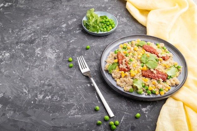 Quinoa Brei mit grüner Erbse, Mais und getrockneten Tomaten auf Keramikplatte auf einem grauen Betonhintergrund. Seitenansicht,