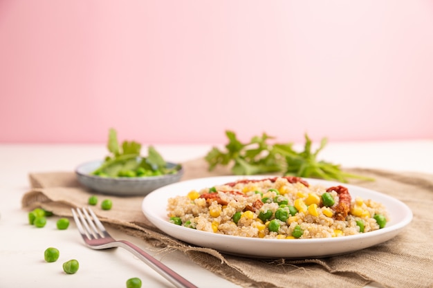 Quinoa Brei mit grüner Erbse, Mais und getrockneten Tomaten auf Keramikplatte auf einem weißen und rosa Tisch