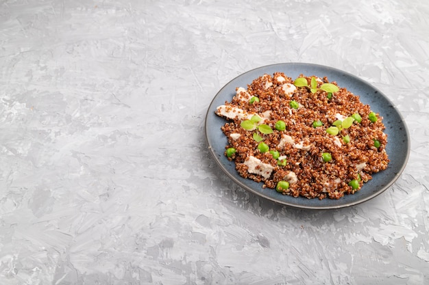 Quinoa Brei mit grüner Erbse und Huhn auf Keramikplatte auf einem grauen Betonhintergrund.