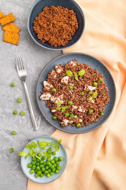 Quinoa Brei mit grüner Erbse und Huhn auf Keramikplatte auf einer grauen Betonoberfläche und orange Textil