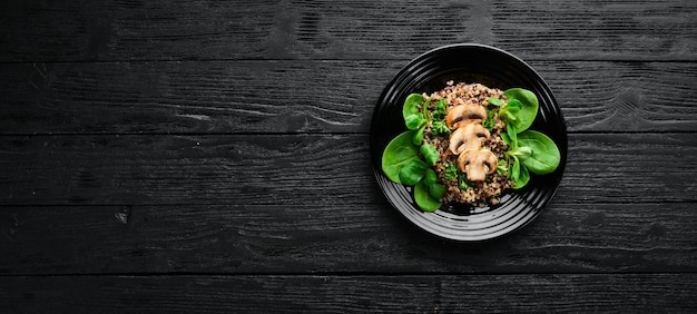 Quinoa com espinafre e cogumelos em um prato preto sobre um fundo de madeira vista superior espaço livre para o seu texto postura plana