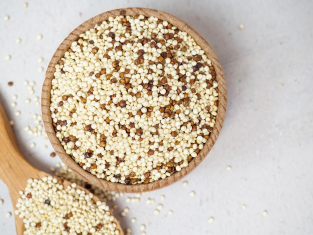 Quinoa misturada crua na tigela e colher sobre fundo claro de concreto. Superalimento saudável e dieta