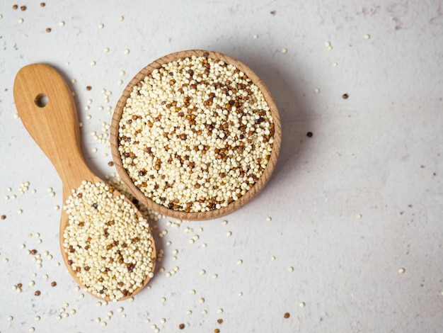 Quinoa misturada crua na tigela e colher sobre fundo claro de concreto. Superalimento saudável e dieta