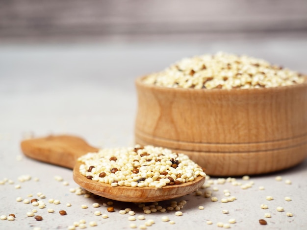 Quinoa misturada crua na tigela e colher sobre fundo claro de concreto. Superalimento saudável e dieta