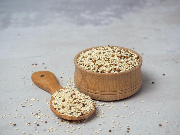 Quinoa misturada crua na tigela e colher sobre fundo claro de concreto. Superalimento saudável e dieta