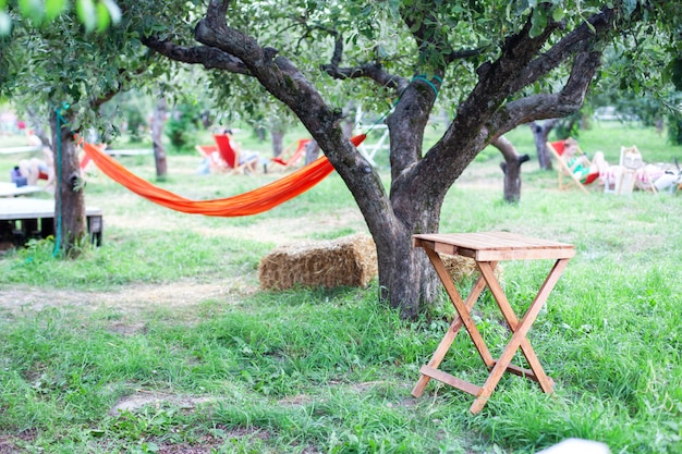 Quintal com rede e mesa de madeira para relaxar. terraço, jardim de maçã no verão, mesa de madeira com palheiro. mesa de madeira no pátio em um dia de outono na vila. relaxando na rede no jardim.