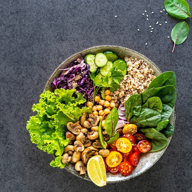 Quinua, champiñones, lechuga, col lombarda, espinacas, pepinos, tomates, un cuenco de Buda sobre una superficie oscura, vista superior. Delicioso concepto de nutrición equilibrada