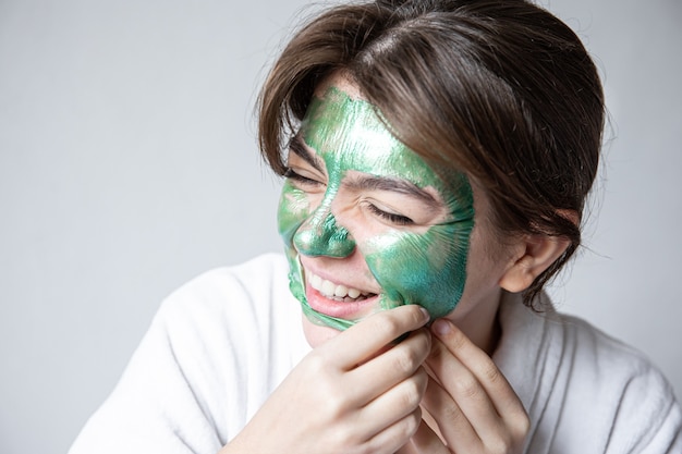 Quitar una mascarilla cosmética verde de la atractiva cara de niña