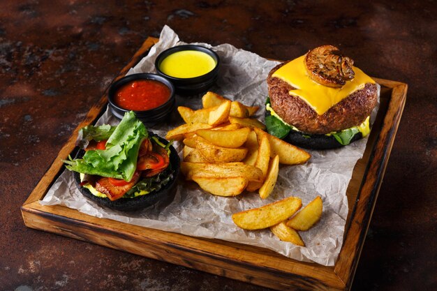 Quitar el menú de hamburguesas en bandeja de madera en el viejo fondo oxidado. Hamburguesa de pan negro con rodajas de papa al horno y salsas, concepto de comida rápida