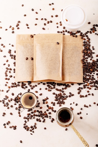 Quite la taza de papel, los granos de café y los paquetes de café con un espacio en blanco para el logotipo sobre la superficie blanca. Copie el espacio. Vista superior