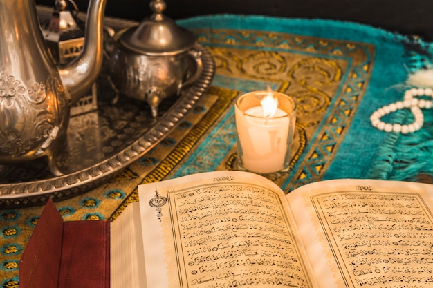 Quran cerca de vela y bandeja con utensilios de cocina