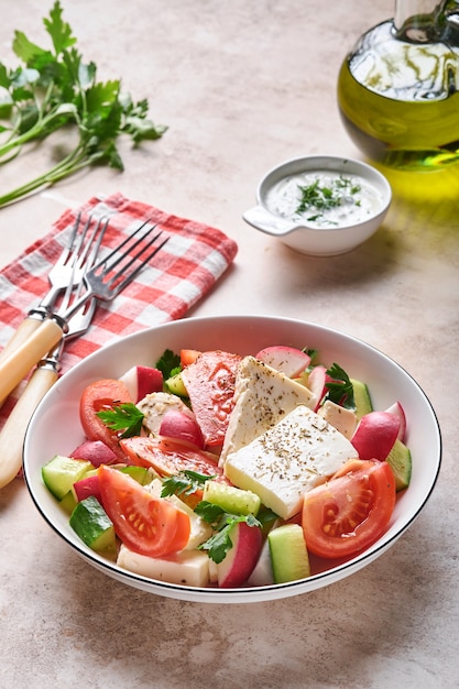 Rabanete, pepino, tomate, pimenta e queijo feta com especiarias pimenta e azeite em uma tigela branca em ardósia cinza, pedra ou fundo de concreto. Conceito de comida saudável. Vista do topo.