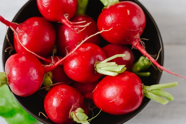 Rabanete vermelho cru fresco em chapa preta sobre fundo branco de madeira