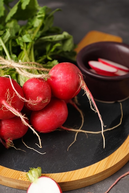 Rabanete vermelho fresco com folhas na tábua sobre fundo cinza verticalmente Fechado