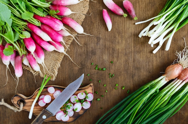 Rabanetes vermelhos frescos cortados e cebolas novas verdes no fundo de madeira branco. dieta saudável com rabanete. ingredientes para uma salada de legumes primavera leve. a vista de cima