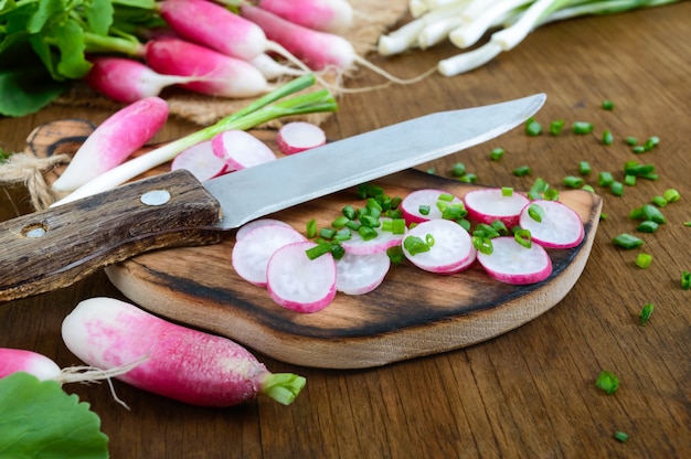 Rabanetes vermelhos frescos cortados e cebolas novas verdes no fundo de madeira branco. dieta saudável com rabanete. ingredientes para uma salada de legumes primavera leve.