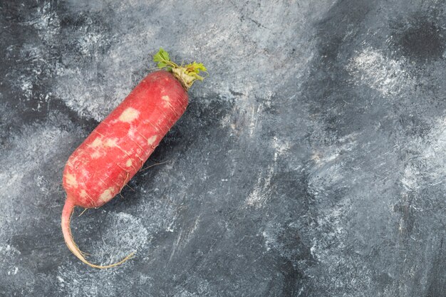 Un rábano rojo entero colocado sobre una mesa de mármol.