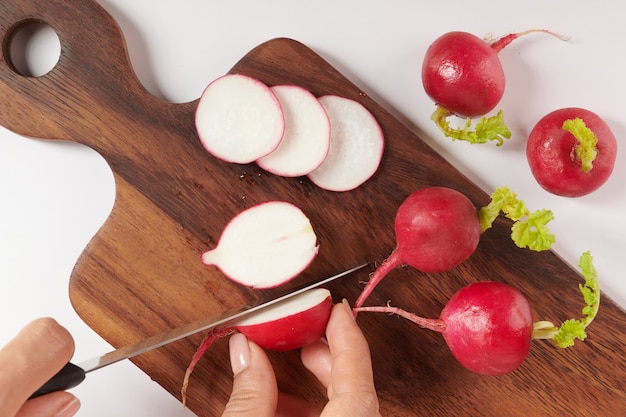 Rábano rojo fresco en la tabla de cortar. Conjunto de rábano pequeño jardín entero fresco aislado en superficie blanca. Vista superior. Endecha plana. Recién recogido del huerto orgánico de crecimiento doméstico. Concepto de comida.